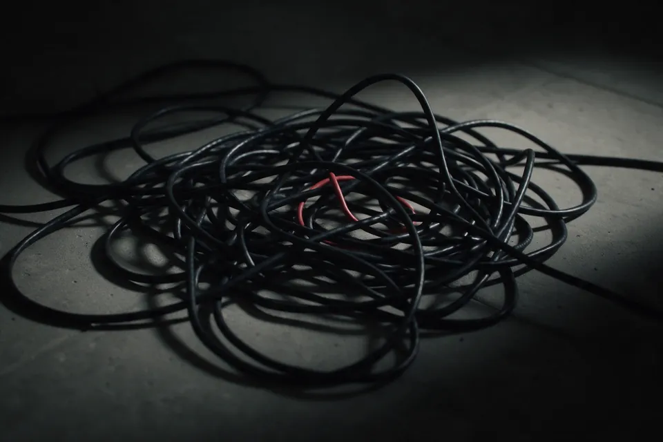 A coil of black cable spilled across a concrete floor in loops and knots, one red cable tangled through it.